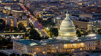 High angle helicopter shot of the Capitol Building in Washington, D.C. at twilight on a clear evening in Fall, with Pennsylvania Avenue beyond.