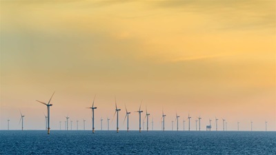 Wind turbines rise from the sea all the way to the horizon under a yellow-orange sky.