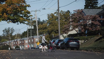 On a clear fall morning, a person pushing a stroller crosses a street lined with cars and rowhomes in a Philadelphia neighborhood.