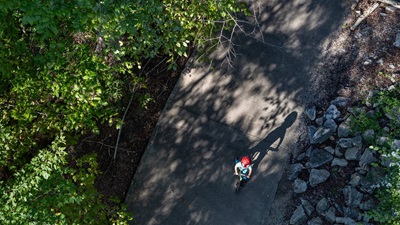 A child wearing a red helmet rides a bicycle on a concrete path with greenery on either side.
